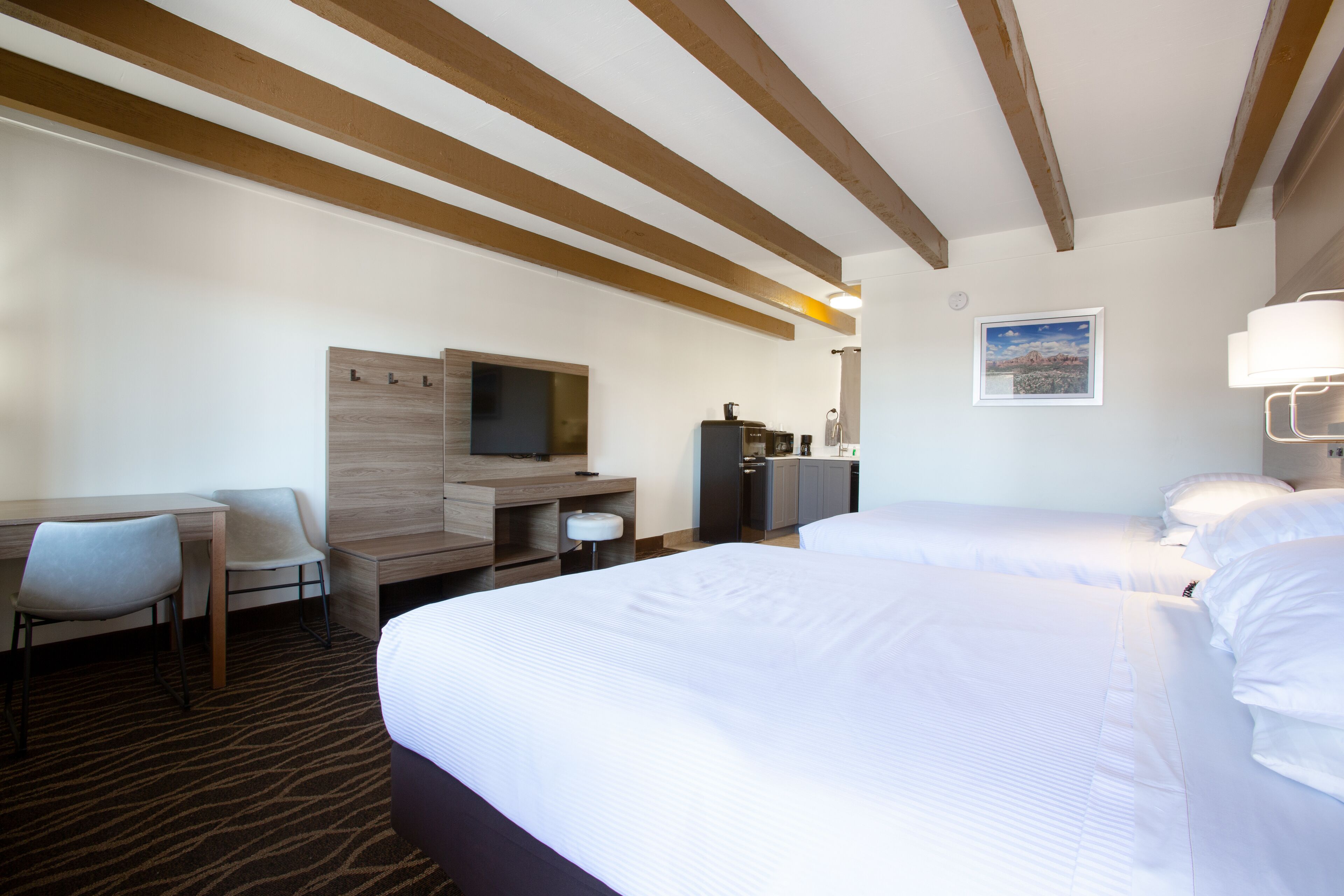 A hotel room with two beds, a desk, a chair, a television, a bathroom, and a framed picture on the wall.