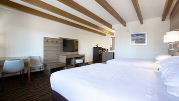 A hotel room with two beds, a desk, a chair, a television, a bathroom, and a framed picture on the wall.