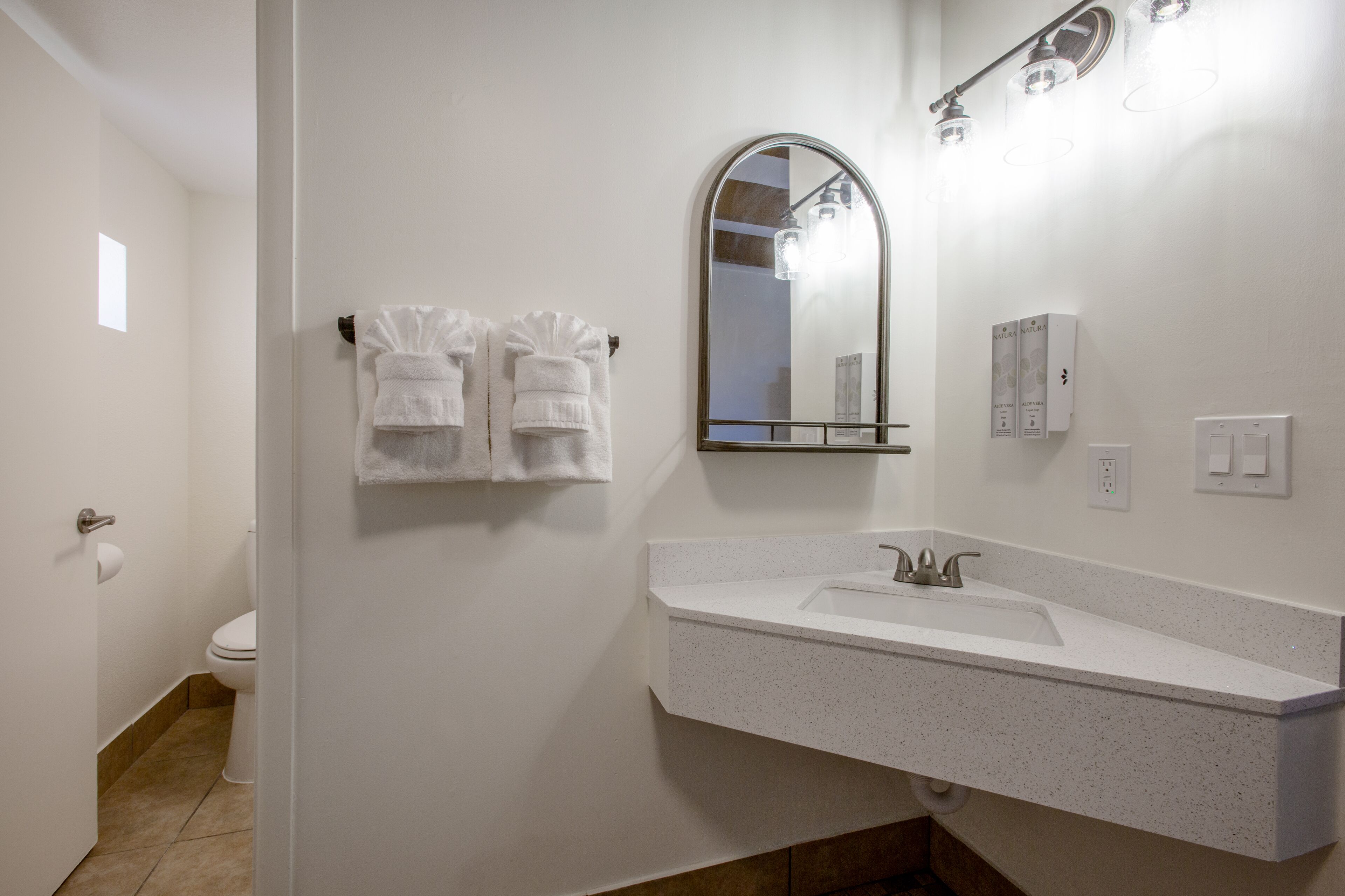 A bathroom with a white sink, a mirror, and two towels hanging on the wall.