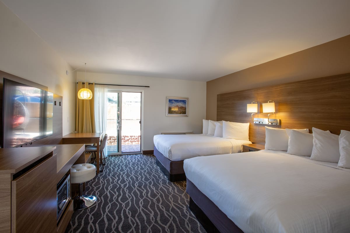 A hotel room with two beds, a desk with a chair, a television, and a large window with curtains.