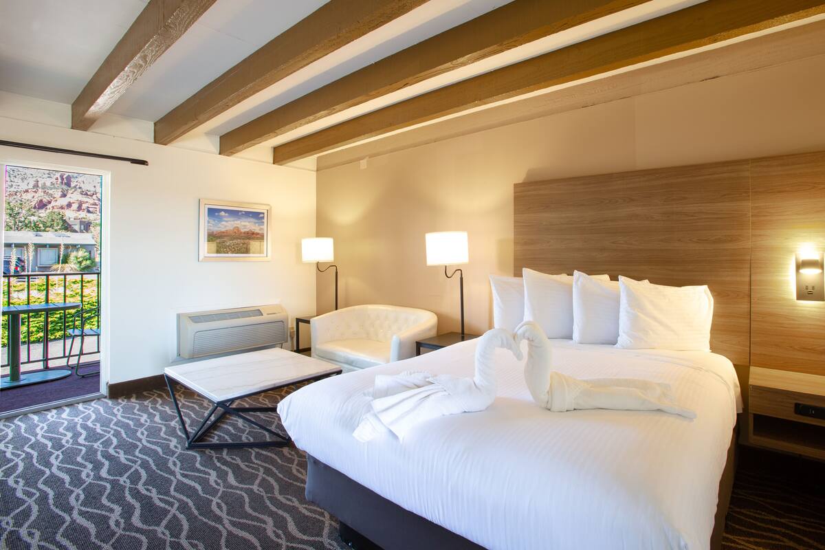 A hotel room with a large bed, two bedside lamps, a chair, a small table, and a view of a balcony with a railing.
