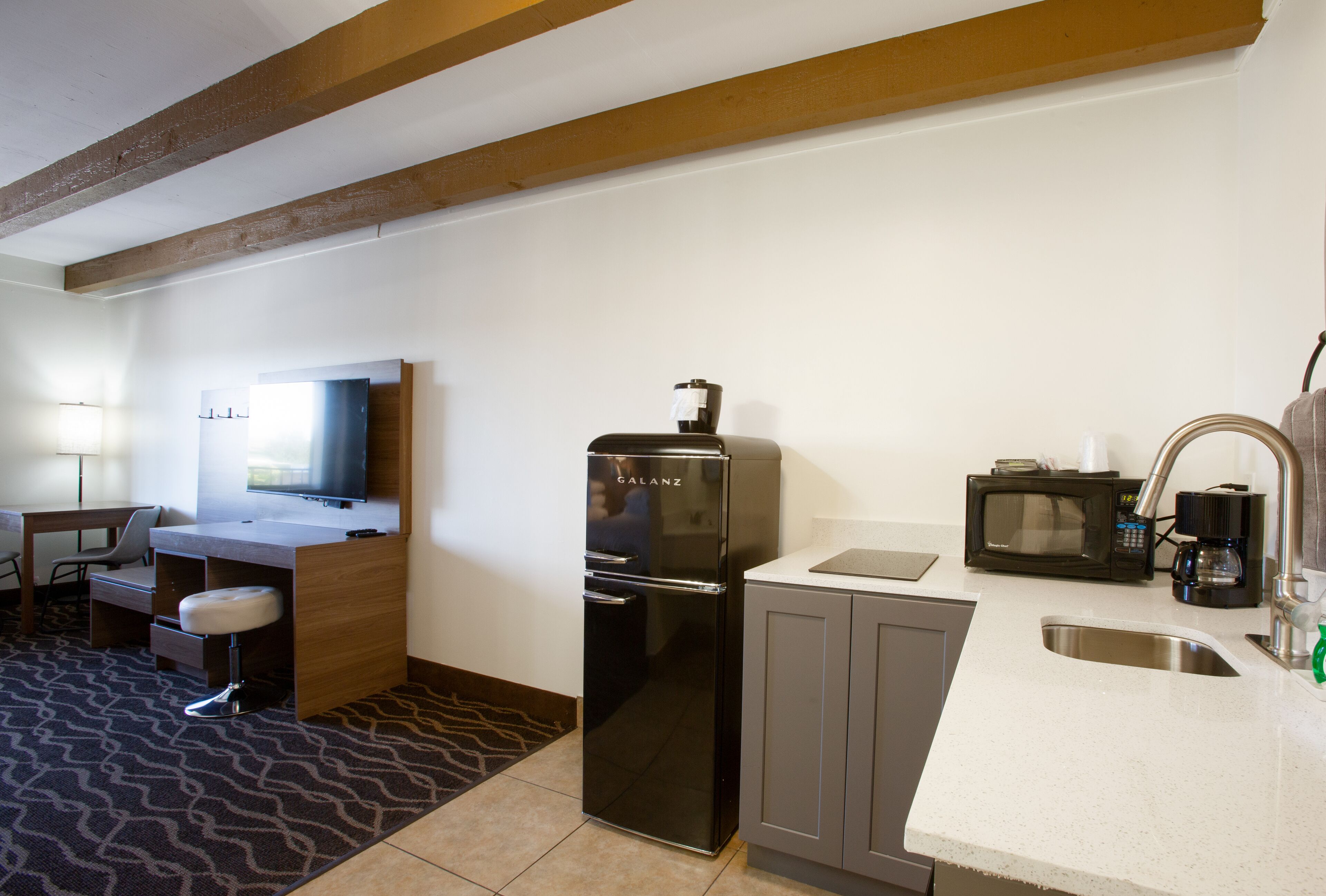 Een compacte hotelkamer met kitchenette, inclusief een koelkast, magnetron en wastafel.