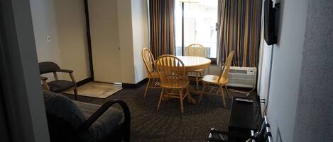 A hotel room with a bed, a small table with chairs, a TV, and a window with curtains.