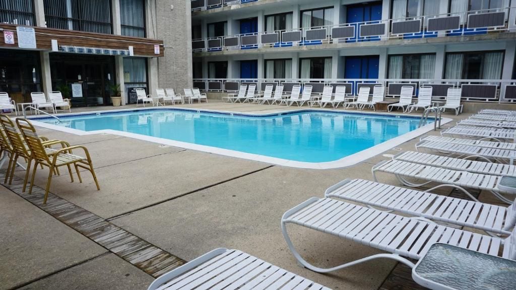 Une piscine avec des chaises longues et, au fond, un bâtiment doté de nombreux balcons.