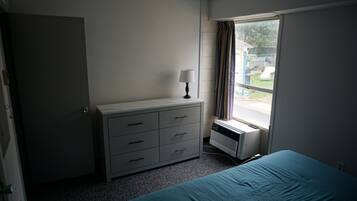 A bedroom with a bed, a dresser, a window with curtains, and a radiator.