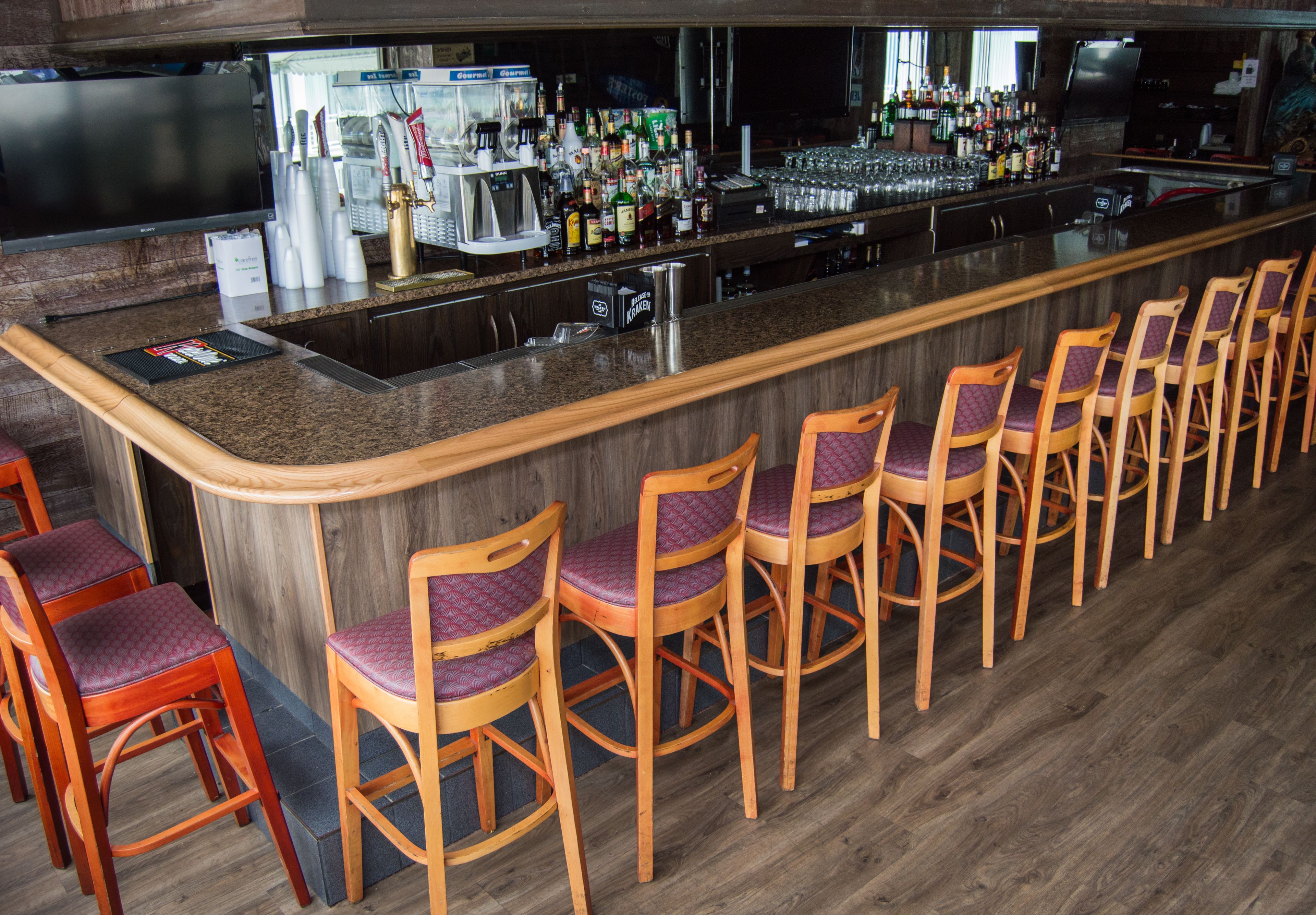 A bar area with wooden bar stools, a counter with various bottles and glasses, and a television screen.