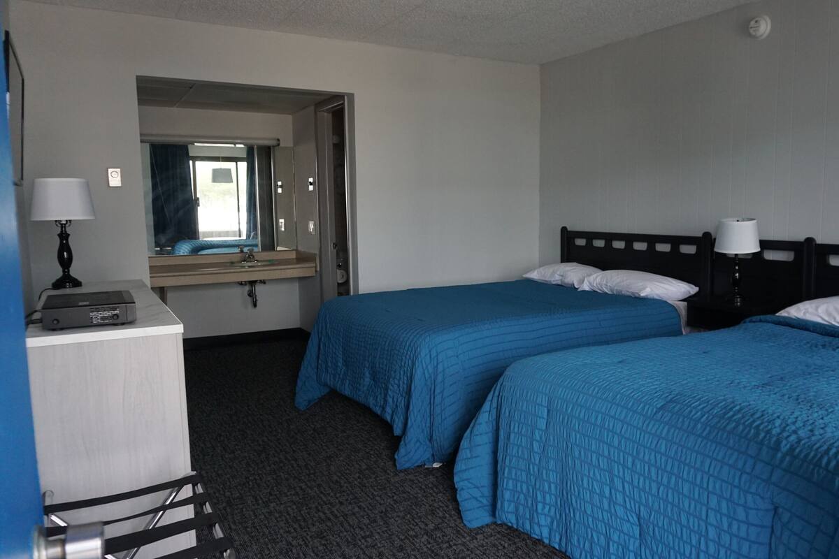 A hotel room with two beds, a desk with a lamp, a mirror, and a window.