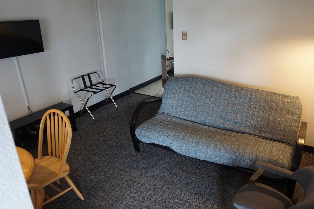 A compact living space with a grey sofa, a wooden chair, a small table, and a wall-mounted TV.