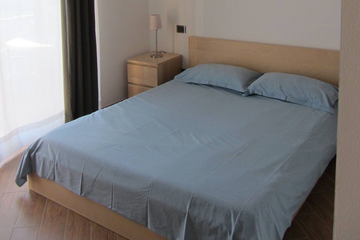 Une chambre à coucher avec un lit en bois, une table de chevet avec une lampe et une fenêtre avec des rideaux.