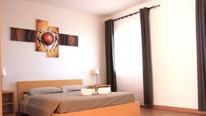 Una cama bien hecha con cabecera de madera, una mesita de noche con lámpara y una obra de arte colgada en la pared.