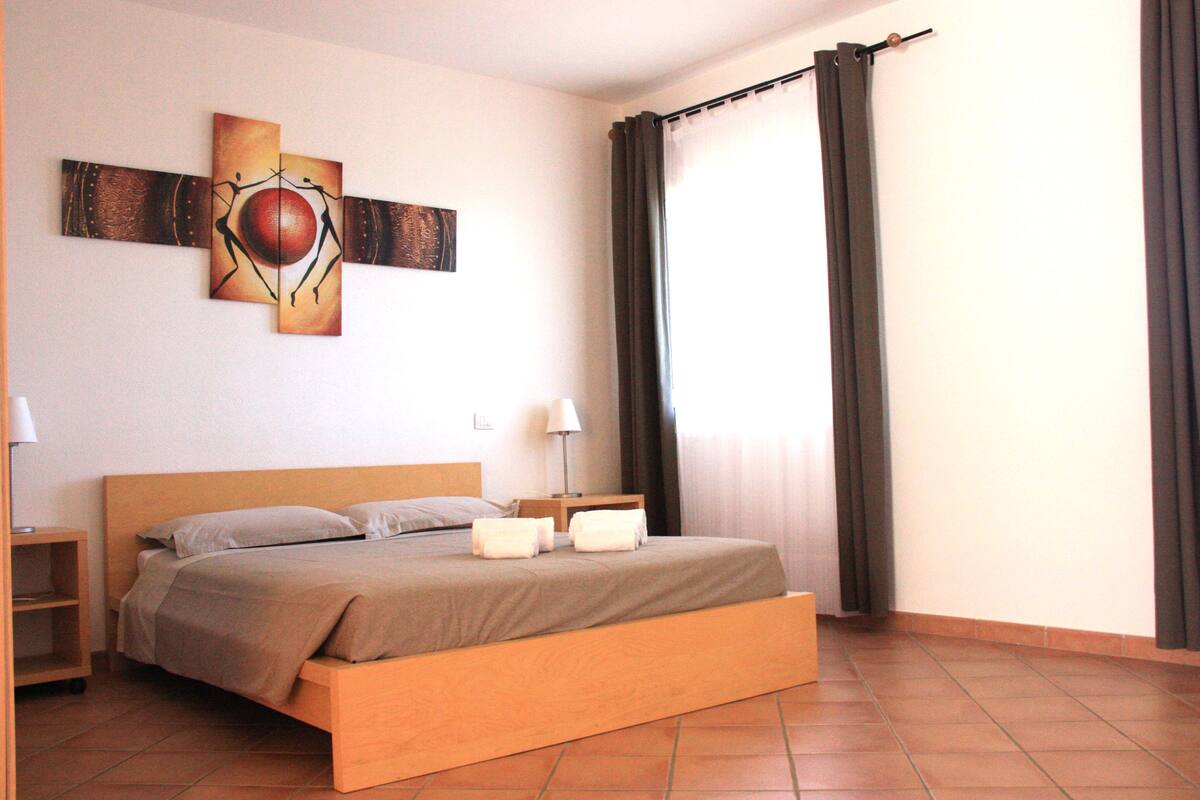 Un lit bien fait, avec une tête de lit en bois, une table de chevet avec une lampe et une œuvre d’art accrochée au mur.