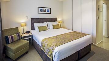A hotel room with a large bed, a chair, two bedside lamps, a framed picture on the wall, and a wardrobe.