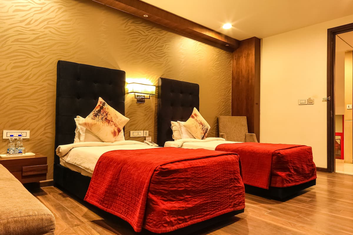 Habitación de hotel con dos camas, cada una con una colcha roja, cabecero de madera y lámpara de pared.