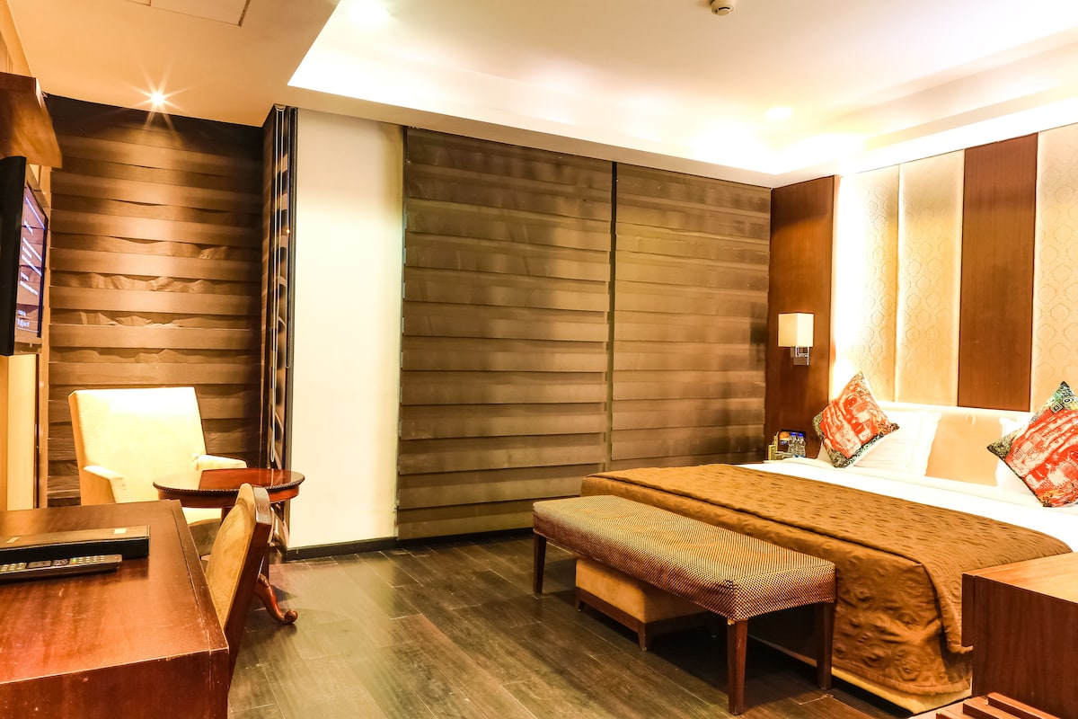 Una habitación de hotel con una cama, un escritorio, una silla, un banco y un ventanal grande.