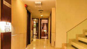 A hotel hallway with directional signs for rooms 101 to 104 and 105 to 106, a staircase, and a door leading to a room with a wooden floor and a table. - The Nanee Suites (New Delhi)