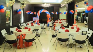 A conference room with round tables, white chairs, and red and blue balloons. - The Nanee Suites (New Delhi)