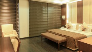A modern hotel room with a large bed, a seating area with a bench, a dining table, and a large window. - The Nanee Suites (New Delhi)