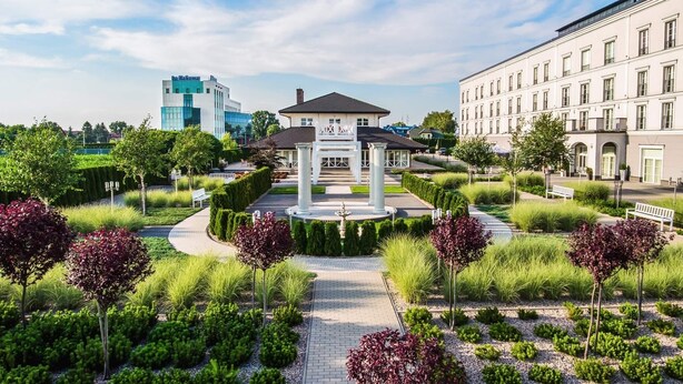 Une cour aménagée avec une fontaine centrale, entourée de haies et d’arbres taillés avec soin.