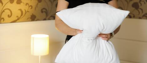 Una persona sosteniendo un almohadón en una habitación con papel tapiz estampado y una lámpara de noche.