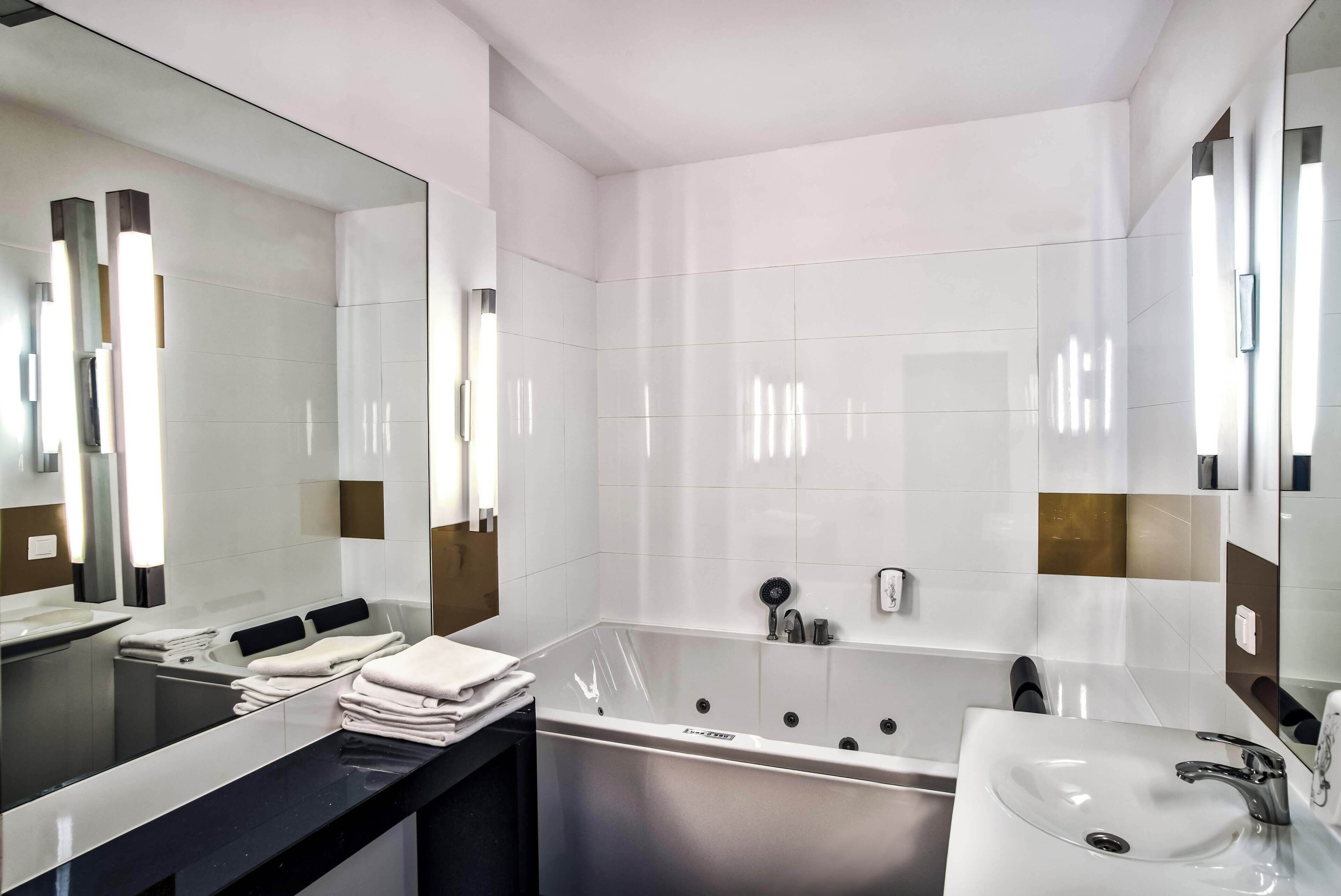 A modern bathroom with a large mirror, a bathtub, a vanity with a sink, and neatly folded towels.