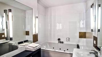 A modern bathroom with a large mirror, a bathtub, a vanity with a sink, and neatly folded towels.