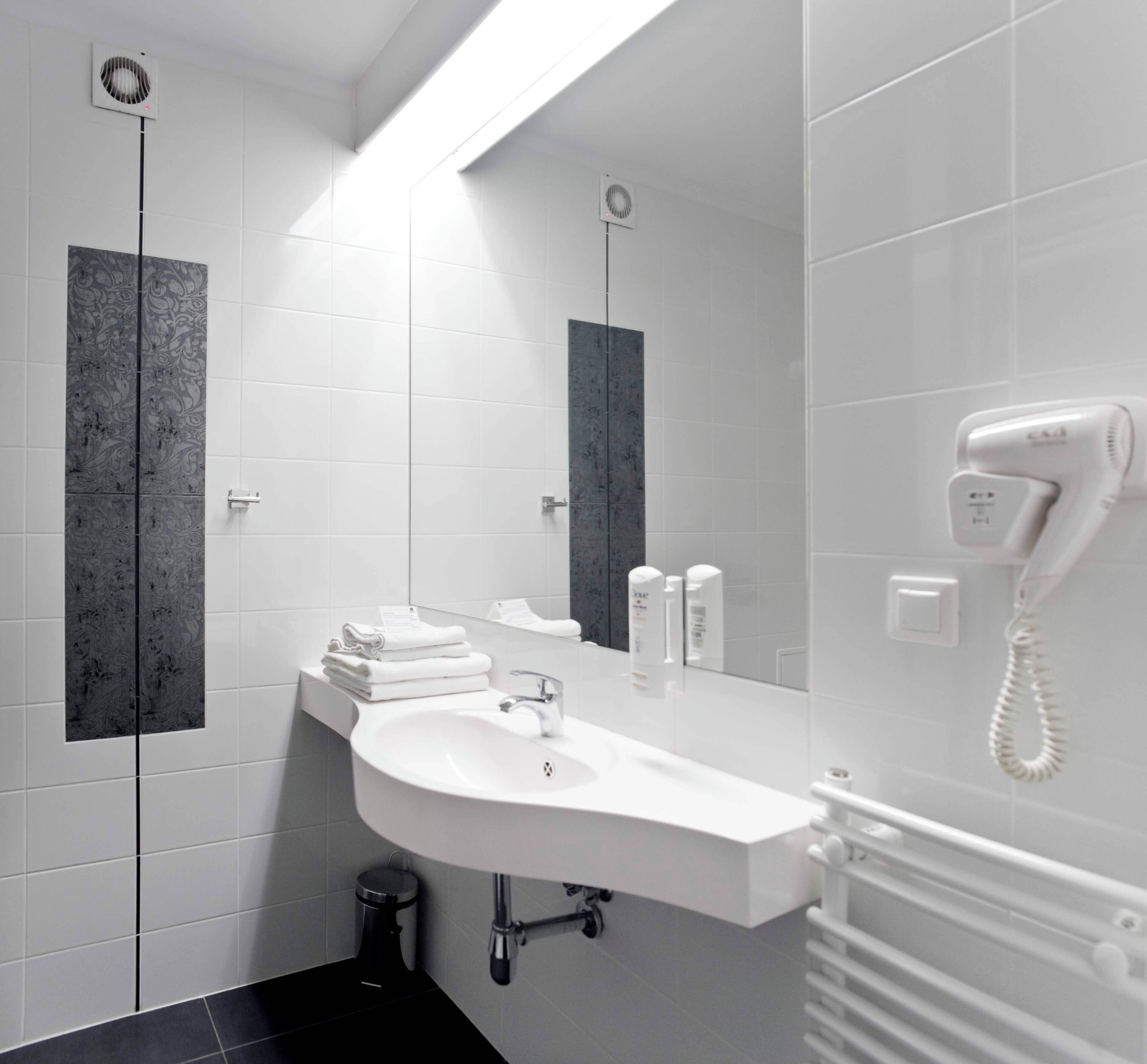 A modern bathroom with a white sink, a mirror, a hairdryer, and a towel rack.