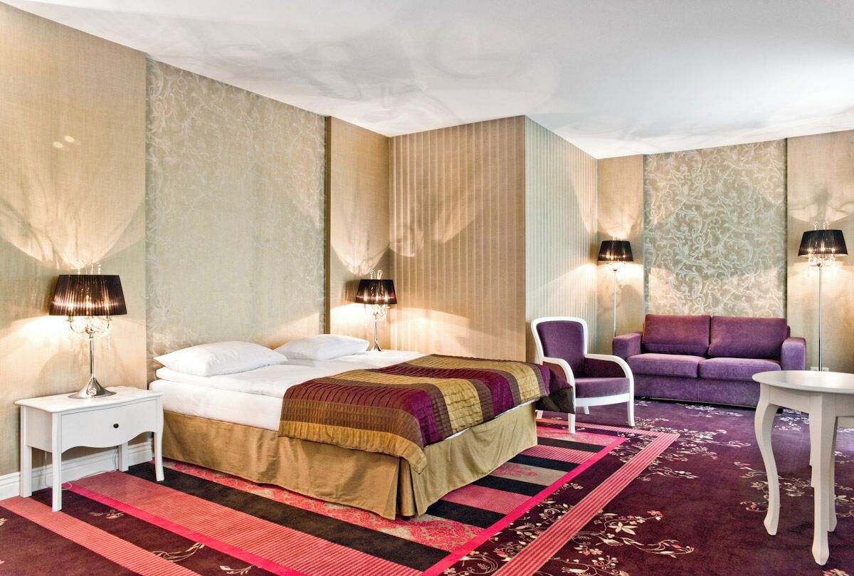 Ein Hotelzimmer mit einem Bett, zwei Sesseln, einer Couch und zwei Lampen.