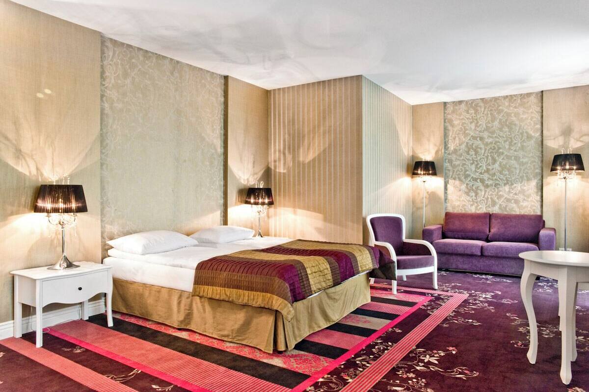 A hotel room with a bed, two chairs, a sofa, and two lamps.