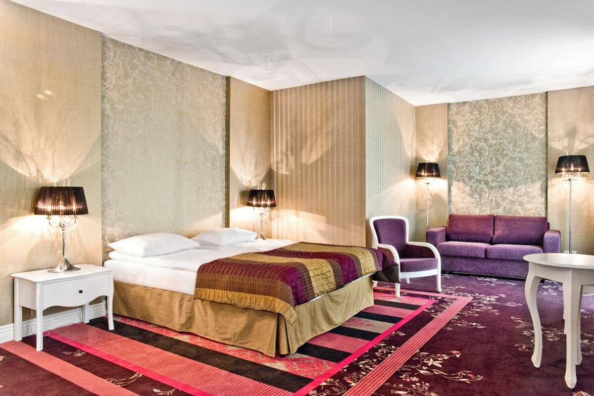 Ein Hotelzimmer mit einem Bett, zwei Sesseln, einer Couch und zwei Lampen.