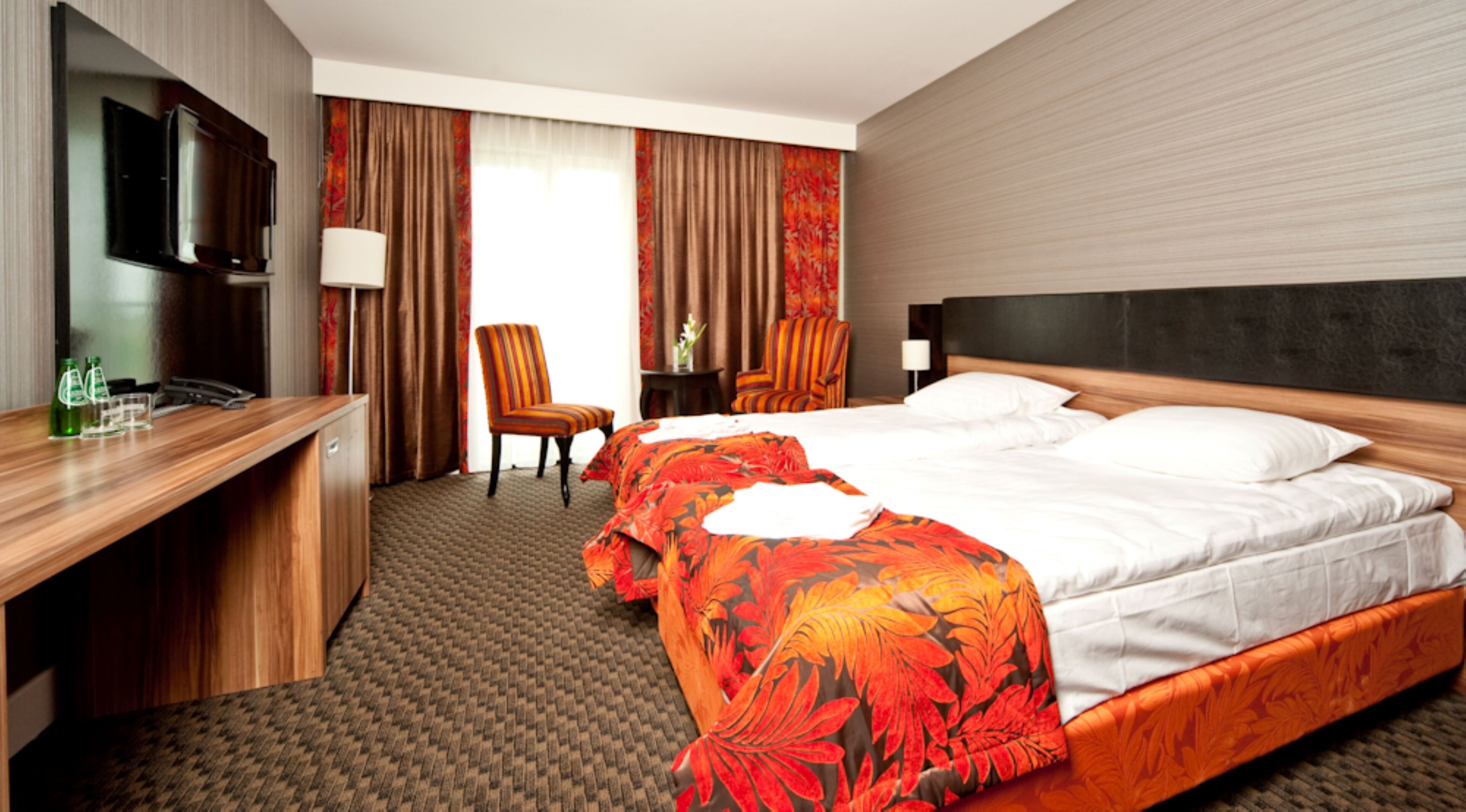A hotel room with a bed, a desk, a chair, a TV, and a window with curtains.