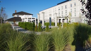 Un hôtel à la façade classique, doté de grandes fenêtres et d’un jardin bien entretenu où poussent de hautes herbes.