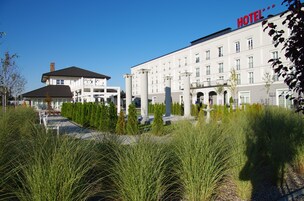 Un hotel con fachada clásica, ventanas amplias y un jardín bien cuidado con hierbas altas.