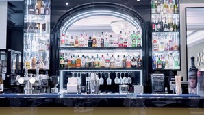 Un espace bar avec des étagères remplies de bouteilles d’alcool, un comptoir de bar équipé de divers ustensiles et un lustre.