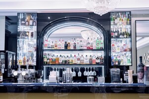 Una zona de bar con estantes llenos de botellas de licores, una barra con distintos utensilios y un candelabro.