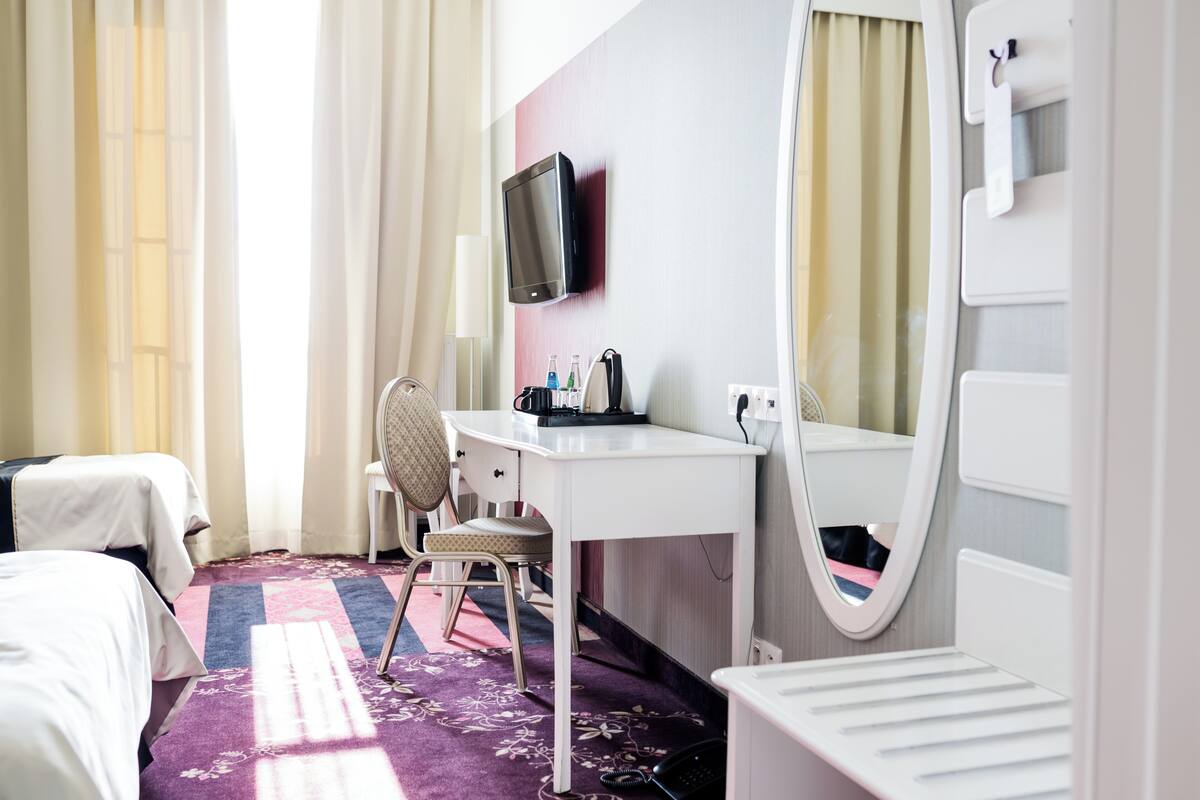 A hotel room with a bed, a desk with a chair, a television, a mirror, and a telephone.
