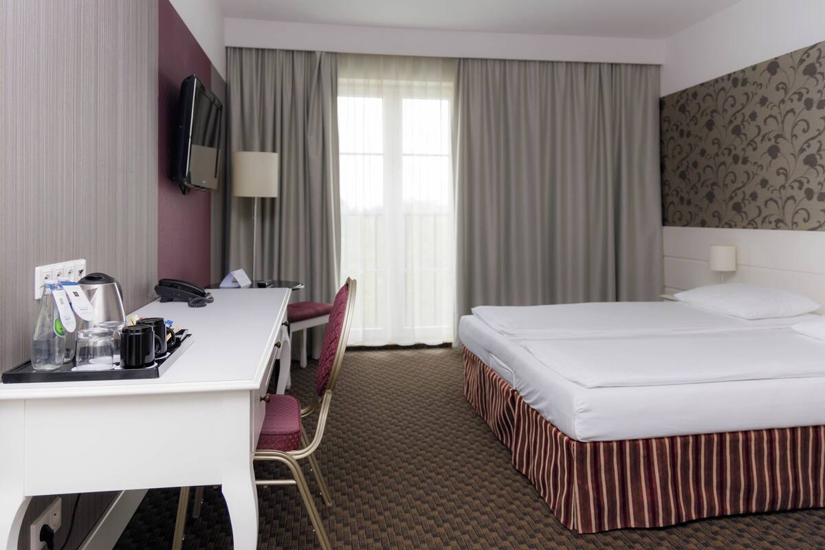 A hotel room with a bed, desk, chair, and a television.