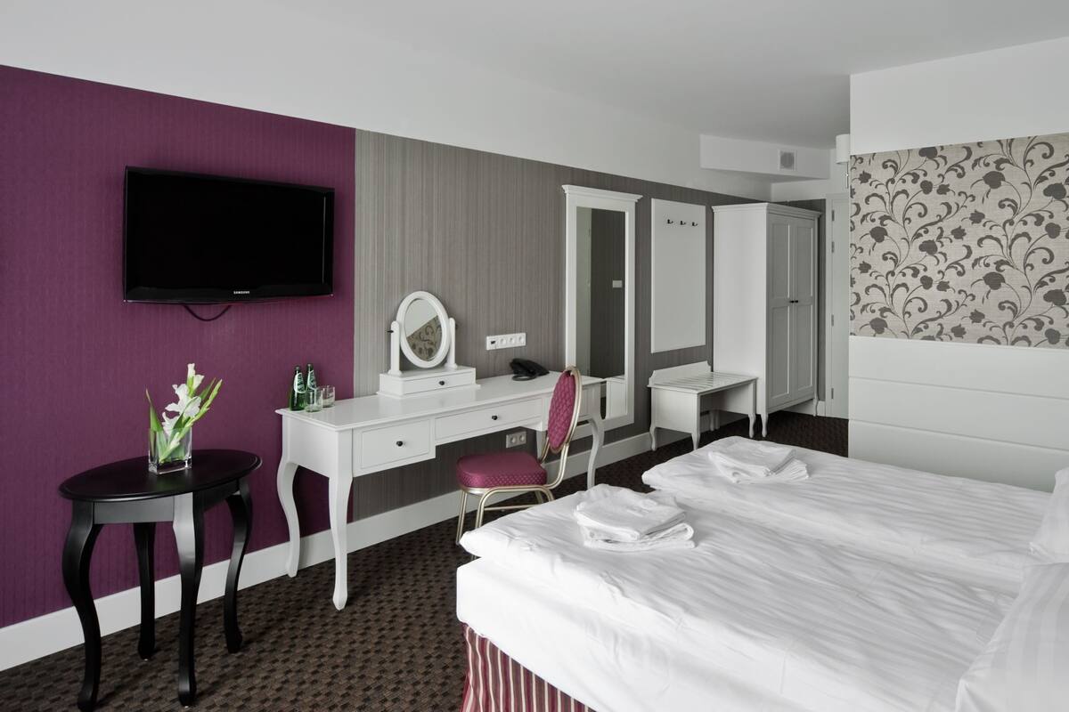 A hotel room with a bed, a desk, a chair, a television, a mirror, and a patterned wall.