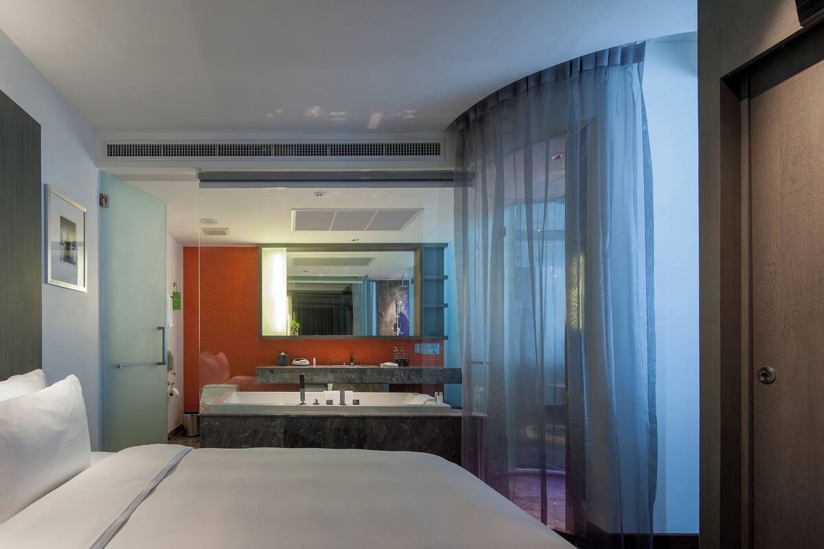 A hotel room with a bed, a bathroom with a sink and mirror, and a door with a curtain.