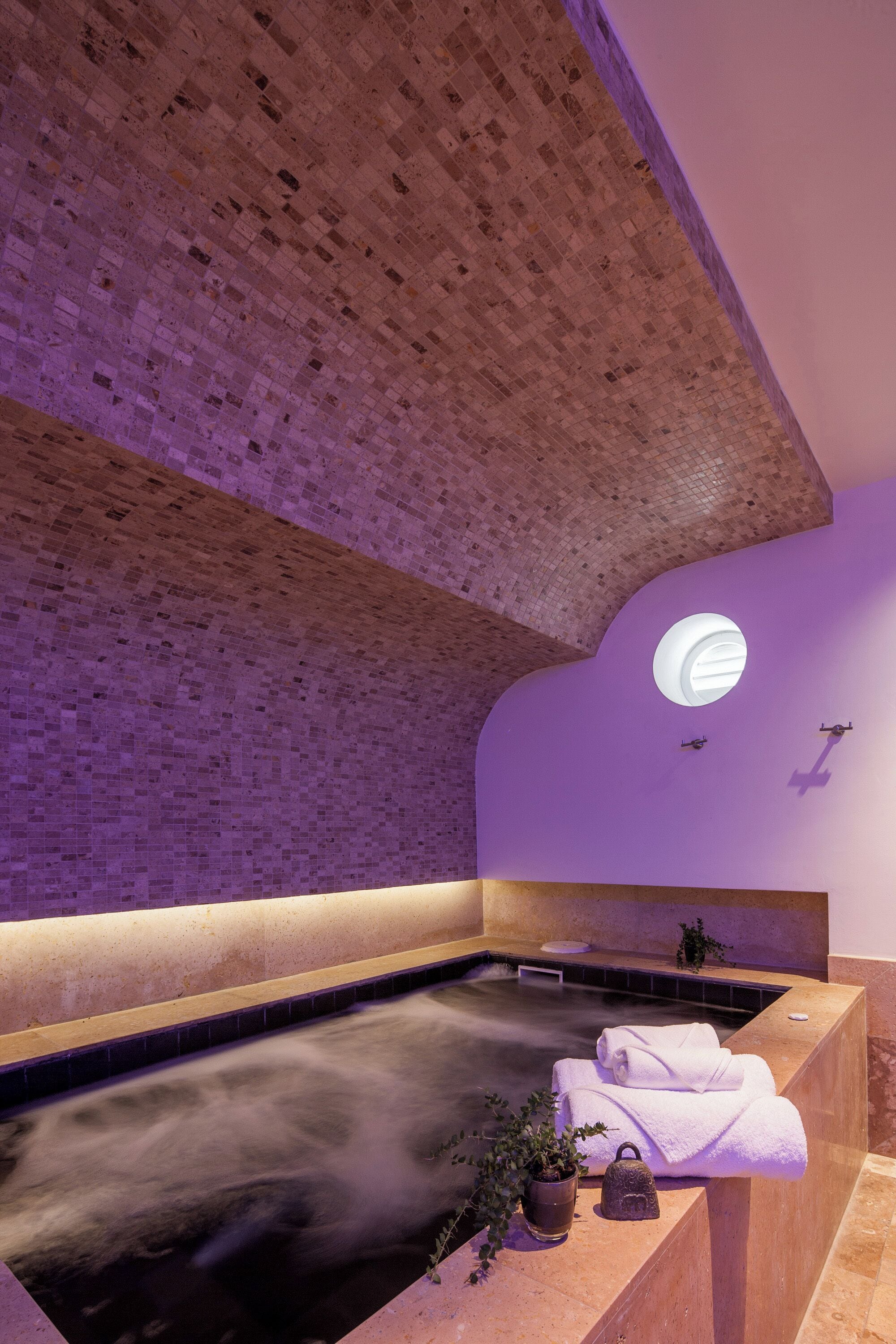 A spa with a brick ceiling, a circular skylight, a hot tub, and towels on a counter.
