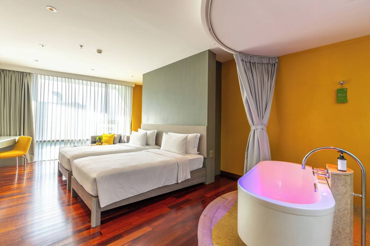 A hotel room with a large bed, a sitting area with a chair, a bathtub, and a window with curtains.