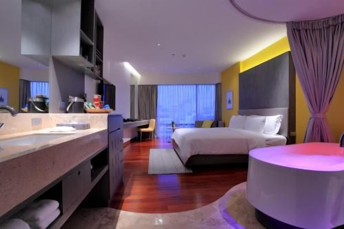 Una habitación de hotel moderna con una cama, un escritorio, una silla y un área de baño.