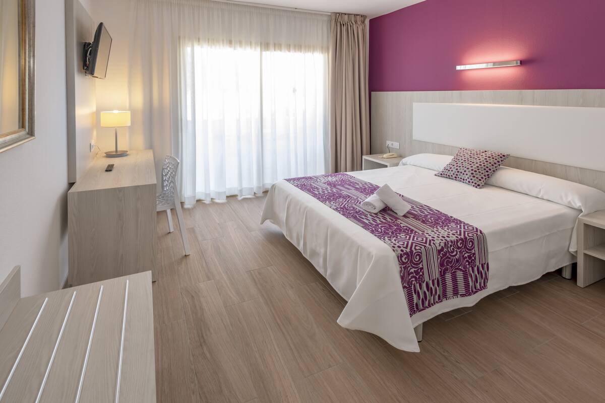 Hotelkamer met een bed, nachtkastjes, een bureau, een stoel, een televisie en een raam met gordijnen.