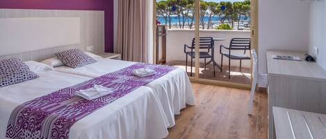 A hotel room with two beds, a balcony with a view of the sea, and a desk.