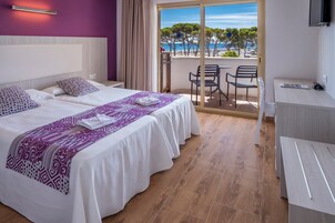 Una habitación de hotel con dos camas, un balcón con vistas al mar y un escritorio.