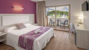 Une chambre d’hôtel comprenant un lit, un bureau, une chaise et un balcon avec vue sur les arbres et le ciel.