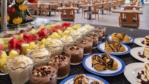 Un bufé con diversos postres y frutas, mesas y sillas en un amplio comedor.