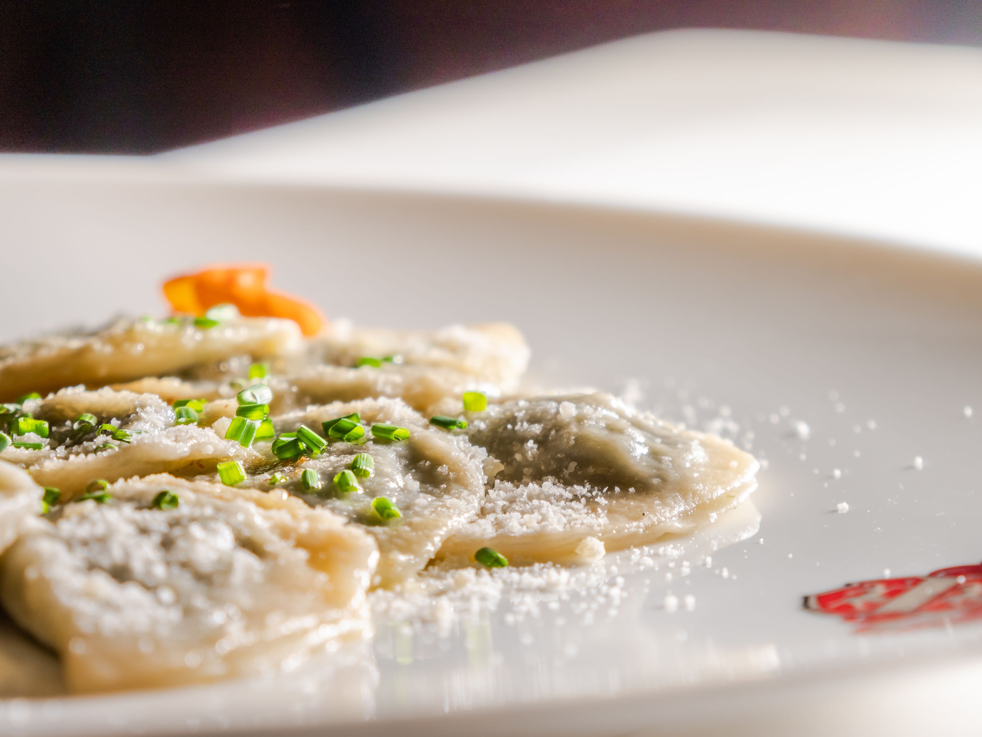 A plate of ravioli garnished with grated cheese and chopped green onions.