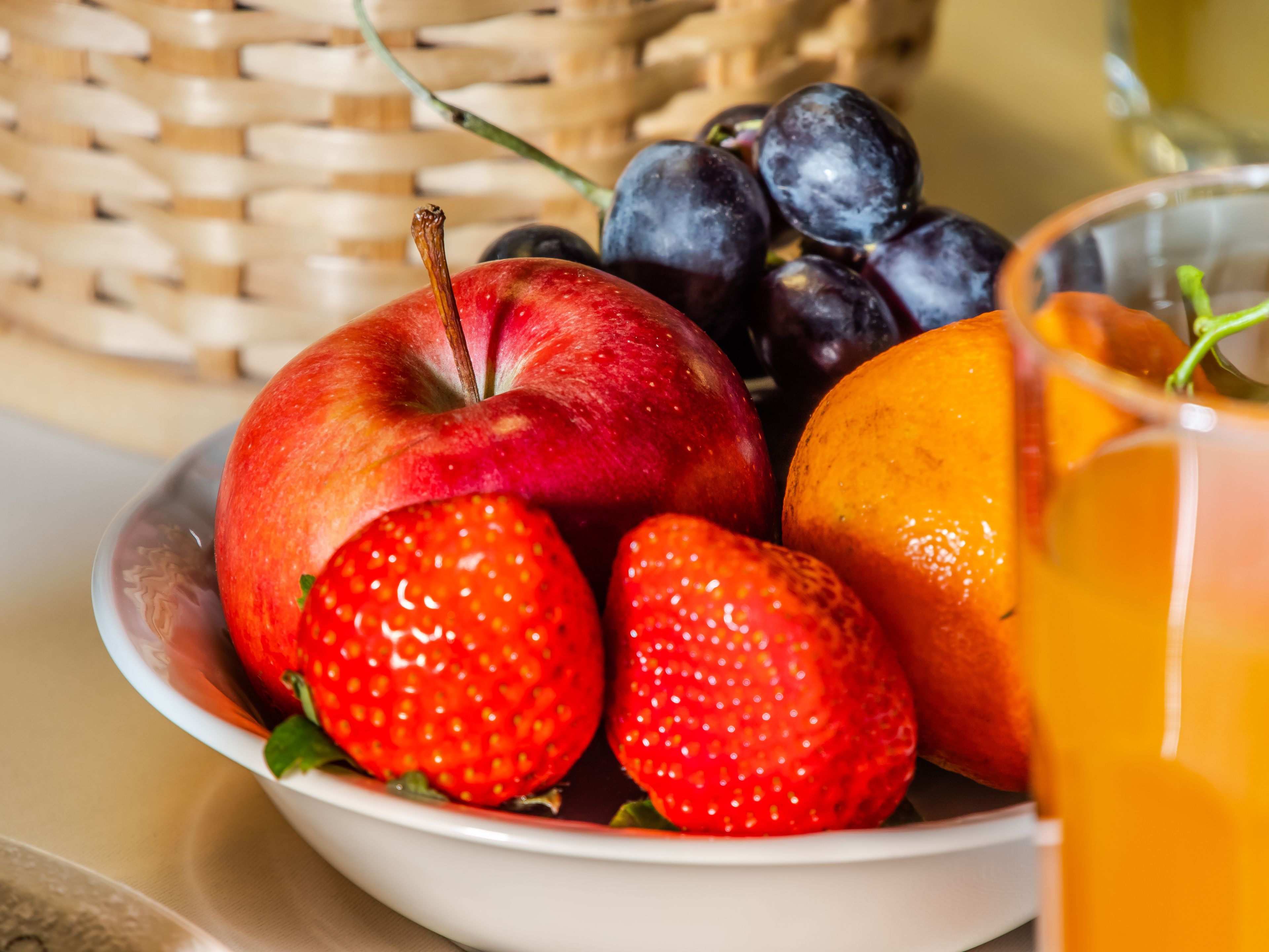 A bowl of fresh fruits including apples, strawberries, and oranges, with a glass of orange juice.