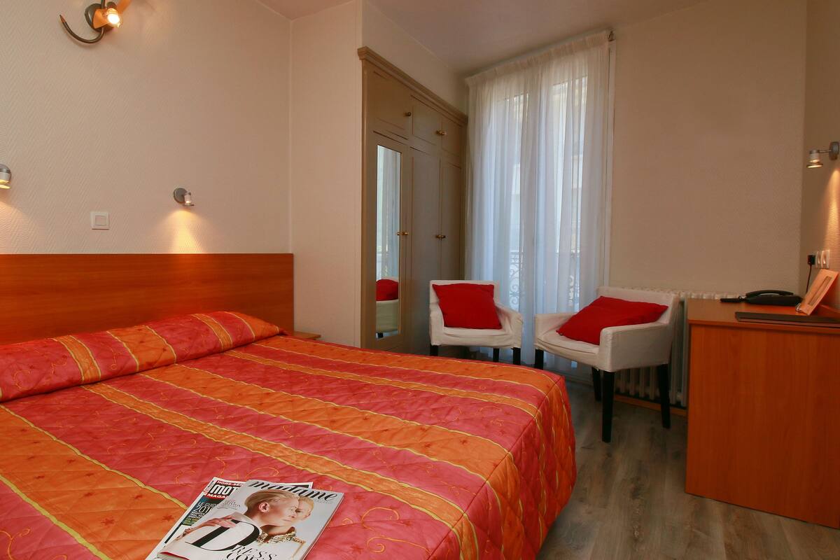 A hotel room with a large bed, two chairs, a desk, and a window with curtains.