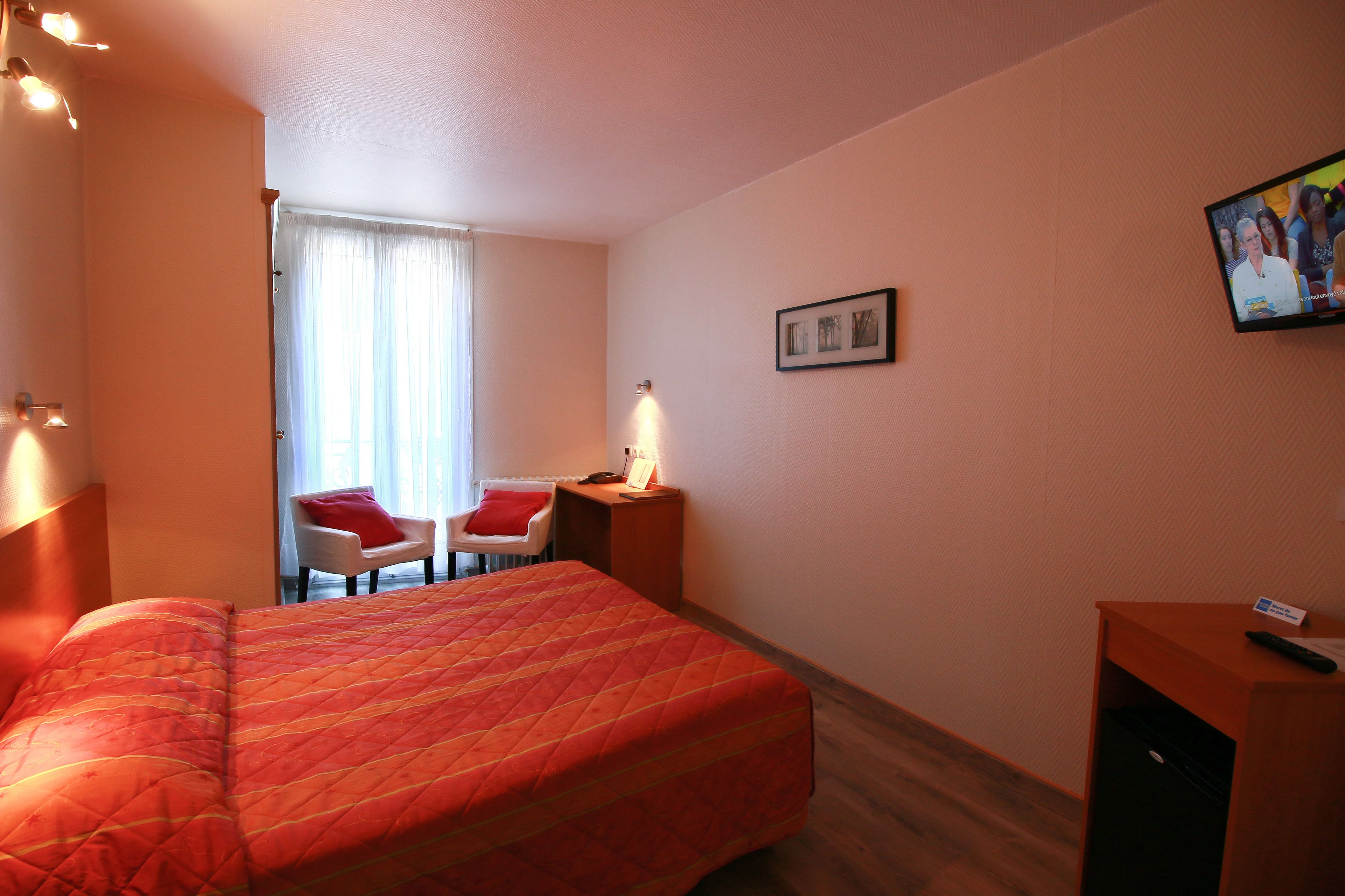 A hotel room with a large bed, a desk with a chair, a television, and a window with curtains.